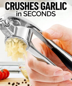 Garlic press placed on cutting board with garlic, ginger, and herbs